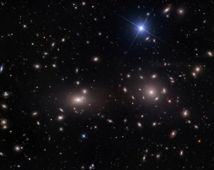 Темная материя — «инопланетяне» для астрофизиков? Две яркие большие галактики в центре скопления Кома, каждая больше миллиона световых лет в размерах. Галактики на окраинах указывают на существование большого ореола темной материи по всему скоплению. Фото.