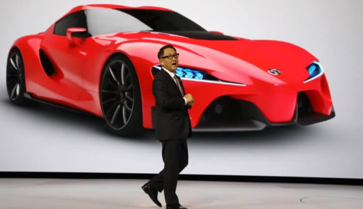 Электрический автомобиль Toyota заряжается за 10 минут. Что о нем еще известно? Глава Toyota Акио Тоеда (Akio Toyoda) на фоне изображения будущего автомобиля. Фото.
