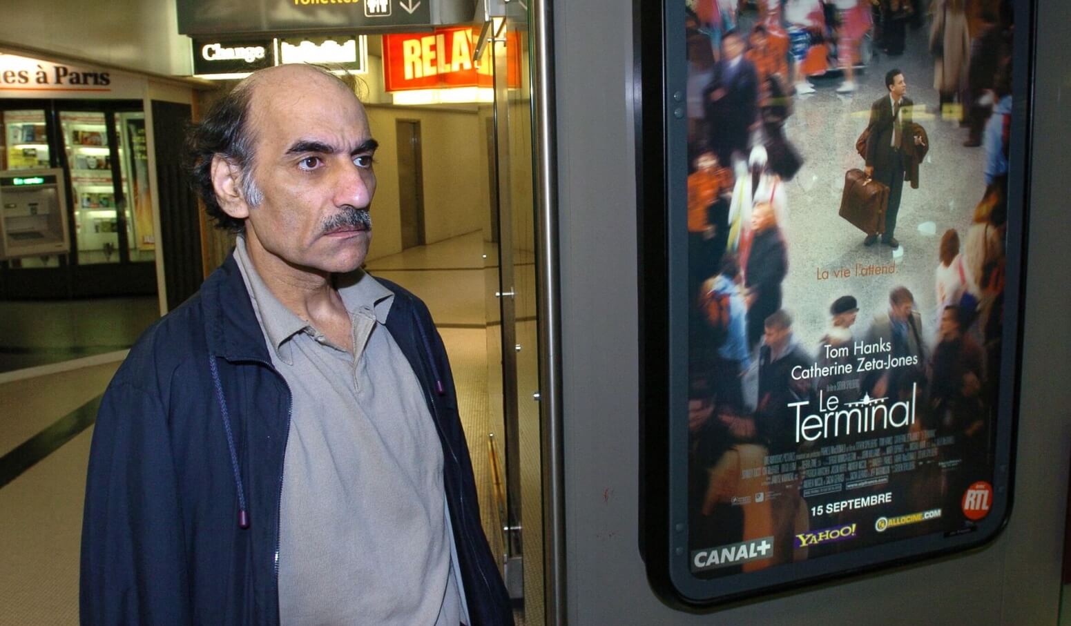 Человек жил в аэропорту 18 лет. Как проходил каждый его день? Мехран Карими Нассери рядом с афишей фильма «Терминал». Фото.