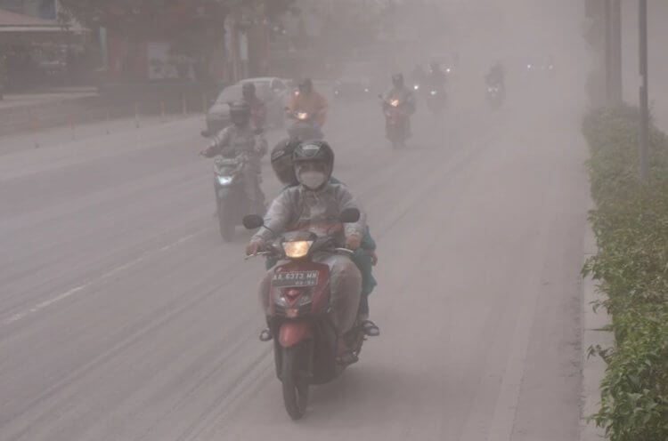 Извержение вулкана Мерапи в 2023 году. Люди едут по дороге, покрытой пеплом вулкана Мерапи. Фото.