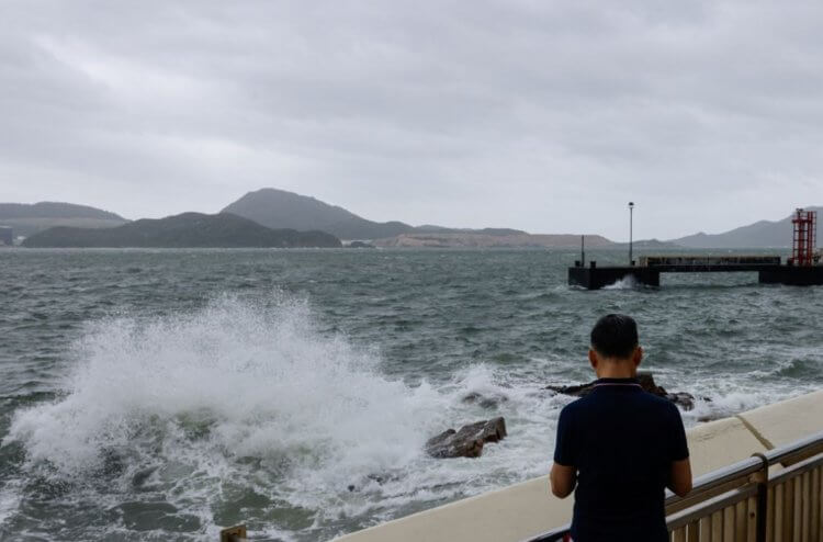 Где находится ветряная электростанция в Китае. Мужчина наблюдает за волнами тайфуна Талим в 2023 году. Фото.
