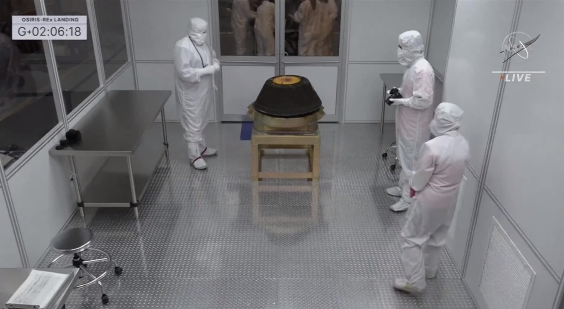 Образцы астероида Бенну доставлены на Землю. Люди в защитных костюмах во время изучения капсулы. Фото.
