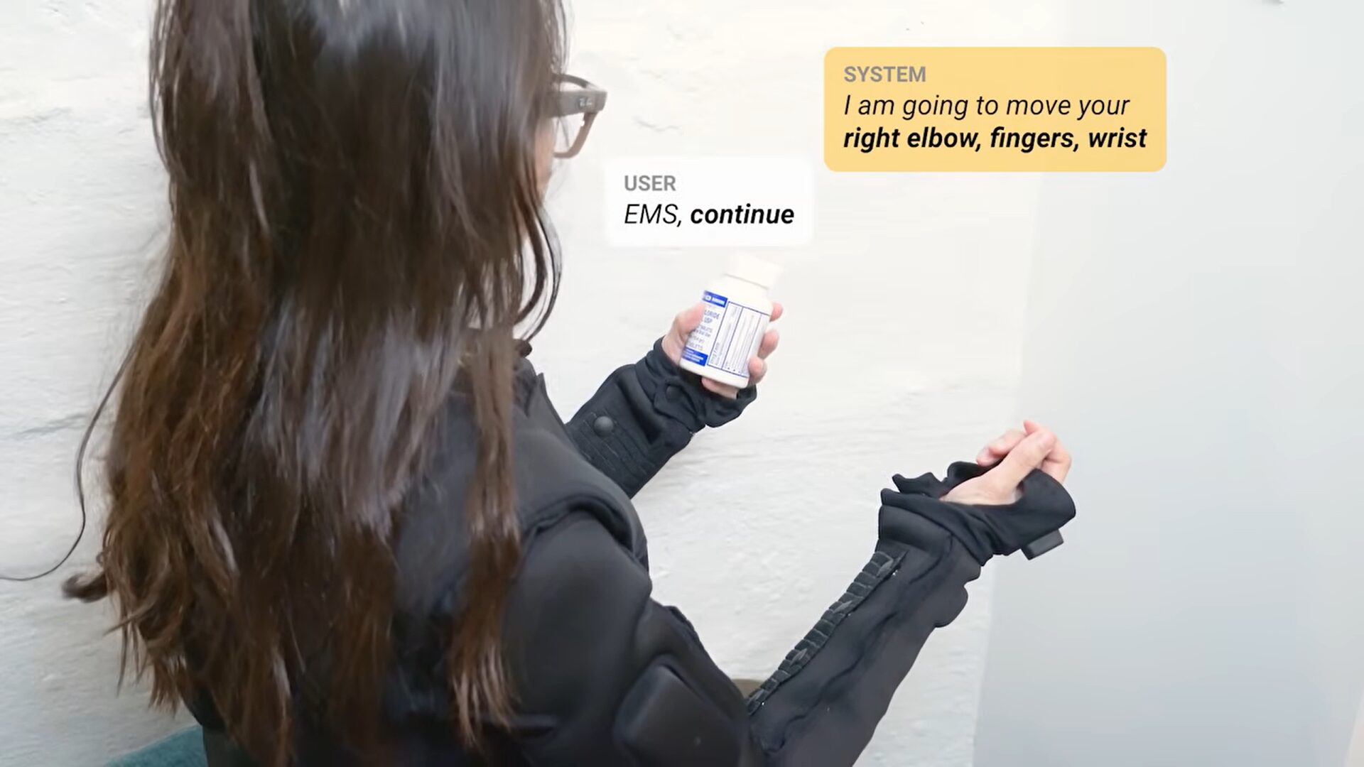 Девушка дала команду «открыть это». Система оценила, ответила, дальше даётся команда «продолжить», после чего костюм открывает банку. Фото.