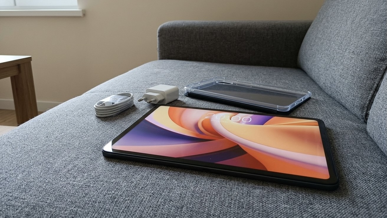 Планшет Teclast на диване, рядом прозрачный чехол, белый блок питания и кабель из комплекта