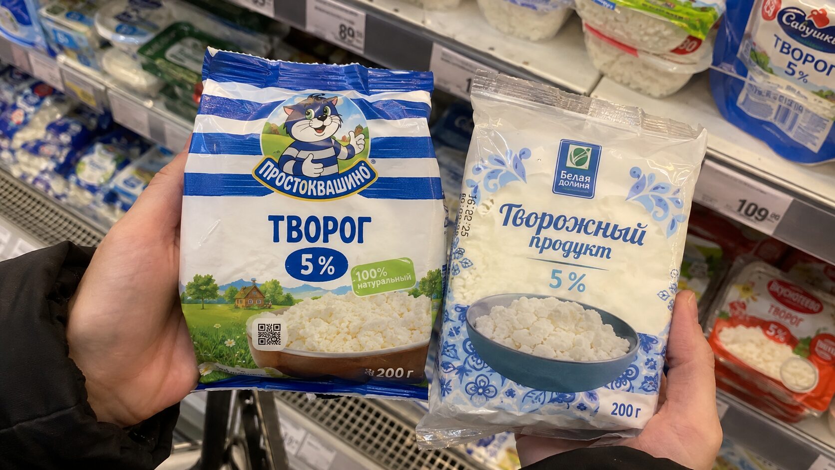 Покупатель сравнивает упаковки творога и творожного продукта в магазине.